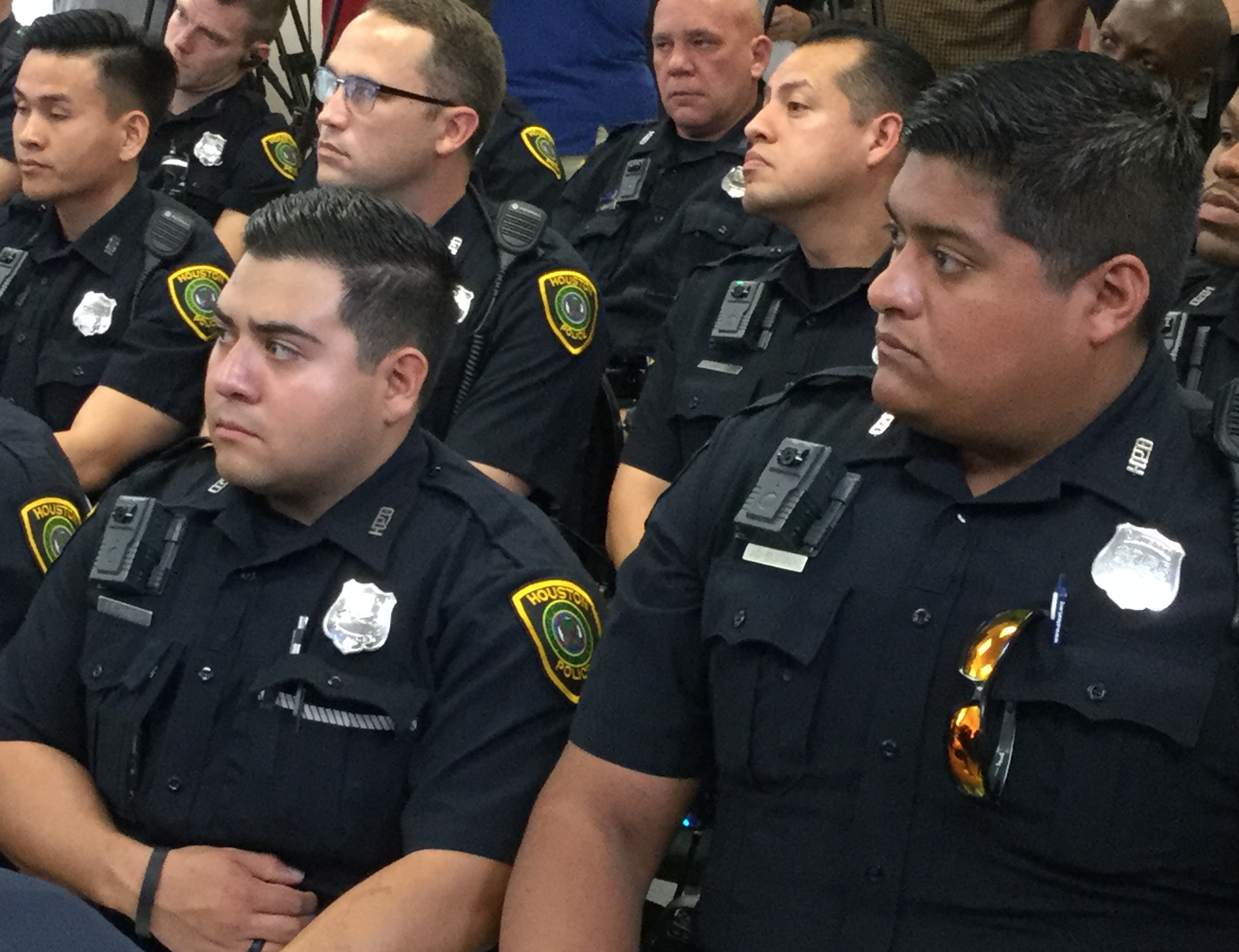 An audience of police officers wearing body cameras on their right shoulders